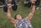 A fit man in his 50s does seated dumbbell bench presses at his yard. Chest workout at home
