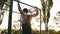 Fit muscular man in black shirt doing pull-ups on horizon bar on sports ground with trees and sun shines on the