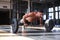 Fit and muscular man doing horizontal push-ups with barbell in gym