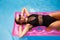 Fit pretty girl in bikini chilling on inflatable pink mattress in swimming pool. Slim hot woman in swimwear tanning