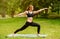 Fit red haired girl doing warrior yoga pose during her outdoor class at park