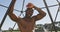 Fit shirtless african american man exercising on climbing frame outdoors, taking a rest