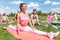 Fit woman doing splits on mat in nature, stretching her legs. Group training outdoors.