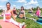 Fit woman doing splits on mat in nature, stretching her legs. Group training outdoors.