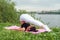 Fit woman making yoga in plow pose on mat in nature.