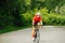 Fit woman riding her racing bike on a road through park with overgrown trees