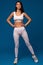 Fit woman in white activewear confidently posing on blue background