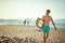 Fit young beardy male walking on the sunny beach, holding surfboard, smiling. Copy space