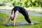 Fit young beautiful woman wearing black sporty leggings working out outdoors in park on summer day, doing Bridge Pose