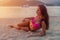 Fit young brunette woman in swimwear lying on beach sunbathing in the setting sun