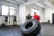 Fit young man with a personal trainer in gym working out, moving tire.