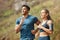 Fit young man and woman running together outdoors. Interracial couple and motivated athletes doing cardio workout while