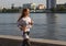 Fit young woman running on the boardwalk along river. Caucasian female athlete training outdoors by waterfront.