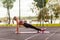 Fit young woman training on mat outdoor summer day, performing reverse plank with foam roller massager