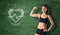 Fitness girl showing her bicep on the background of a chalkboard with drawn beating heart and sport doodles