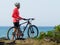 Fitness man with a bicycle stands on the ocean shore and looks into the distance on a sunny day.