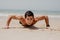 Fitness man doing push-up exercise on beach. Portrait of fit guy working out his arm muscles and body core with pushup exercises o