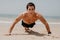 Fitness man doing push-up exercise on beach. Portrait of fit guy working out his arm muscles and body core with pushup exercises o