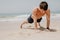 Fitness man exercising push ups smiling happy. Male fitness model cross-training on beach.