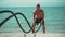 Fitness man training with battle rope on the beach in Eco gym