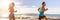 Fitness runners couple doing running exercise run at beach sunset banner panorama. Healthy sports lifestyle panoramic