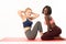 Fitness trainer help doing exercise. Two young international muscular sportswomen doing pair exercise in sports club