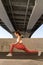 Fitness and wellbeing: young yogi woman working out outdoor under bridge. Slim fit female exercising