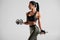 Fitness woman doing exercise for biceps on gray background. Muscular woman workout with dumbbells