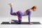 Fitness woman doing kickback exercise for glutes with resistance band on gray background. Athletic girl working out donkey kicks