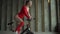 Fitness woman in red bodysuit exercising on stationary cycling machine in gym