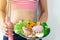 Fitness woman with sport equipment holding plate of healthy food