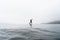 Fitness woman standing on surfboard enjoying supsurfing with paddle at endless sea water fog