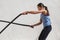 Fitness woman training battle ropes workout at gym. Girl working out arms and cardio using battling rope for cross fit