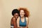 Fitness Women. Ethnic Girls Portrait. Hugging African Brunette And Caucasian Redhead On Beige Background.