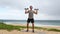 Fitness workout - man doing Shoulder Press with dumbbells exercising on beach