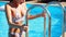 Fitted beautiful girl in wet swimwear climbs out the swimming pool by ladder with handrails. Young woman crawl out of