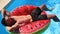 Fitted man in shorts relaxing on floating watermelon water ring. Friends chilling on floaties in private villa swimming