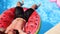 Fitted man in shorts relaxing on floating watermelon water ring. Friends chilling on floaties in private villa swimming