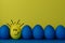 Five blue and one yellow funny faced painted Easter eggs stand on a yellow with blue background. Creative Easter concept