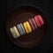 Five colored macarons on the brown plate and pattern background