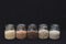 Five different types of cereals in jars on a black background. Porridge. Healthy food