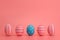 Five Easter blue and pink eggs with white stripes on pink background.