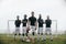 Five football players standing in a formation in front of goalpost. Soccer player standing with one foot on ball with teammates