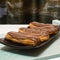 Five fresh eclairs covered with chocolate glaze lie on a rectangular platter.