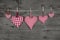 Five handmade red checkered hearts on wooden grey background.