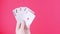 Five of a kind Poker Game cards in gambler hand falling money bills pink background. Lucky combination Aces and Joker revealing 4K