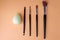 Five makeup brushes lie parallel, brushes for eyeliner, eyeshadow, lipstick, blush and foundation sponge