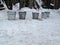 Five metal buckets stand on the snow in a rural yard