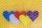 Five multicolored valentine hearts are packed with a transparent bubble wrap on a yellow background. Concept fragility of love