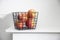 Five red apples in a black metal storage basket that stands on a white mantel